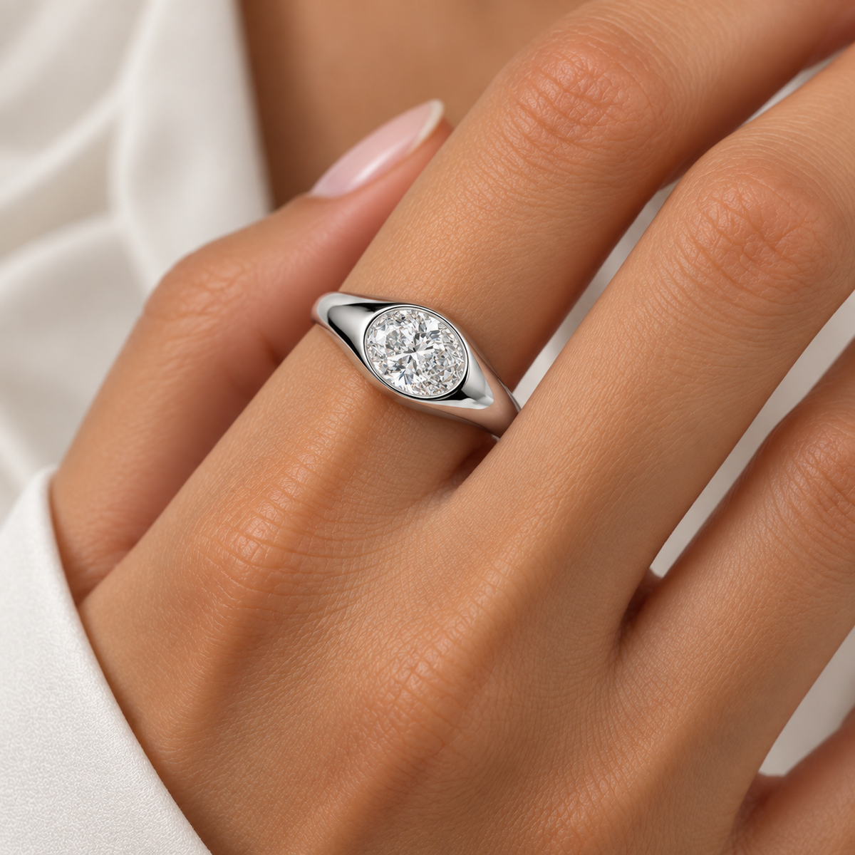 A close-up of a silver oval engagement ring with a round-cut clear diamond, worn on a person's finger.