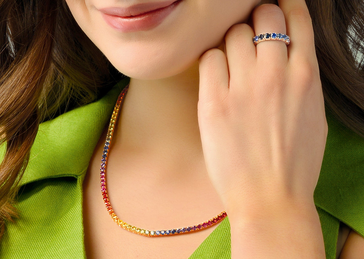 Woman wearing a colorful necklace, ring, and bracelets against a green background
