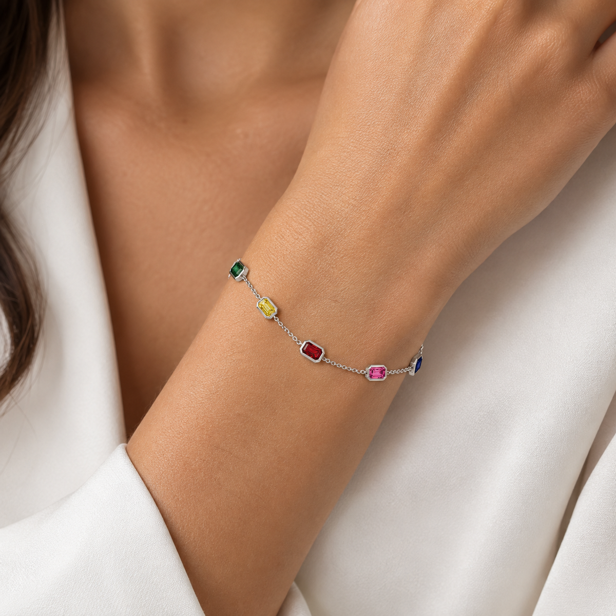 A delicate silver chain bracelet with multiple small, colorful rectangular gemstones, shown worn on a woman's wrist.