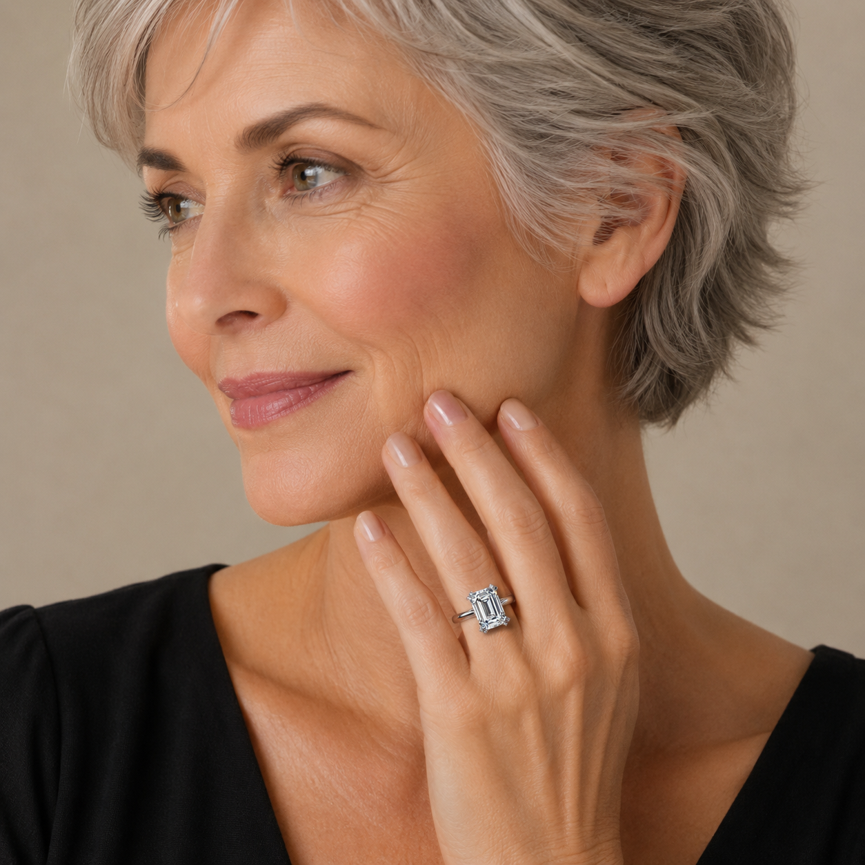 Woman with short gray hair wearing a black top, holding her hand near her face, with a neutral background.