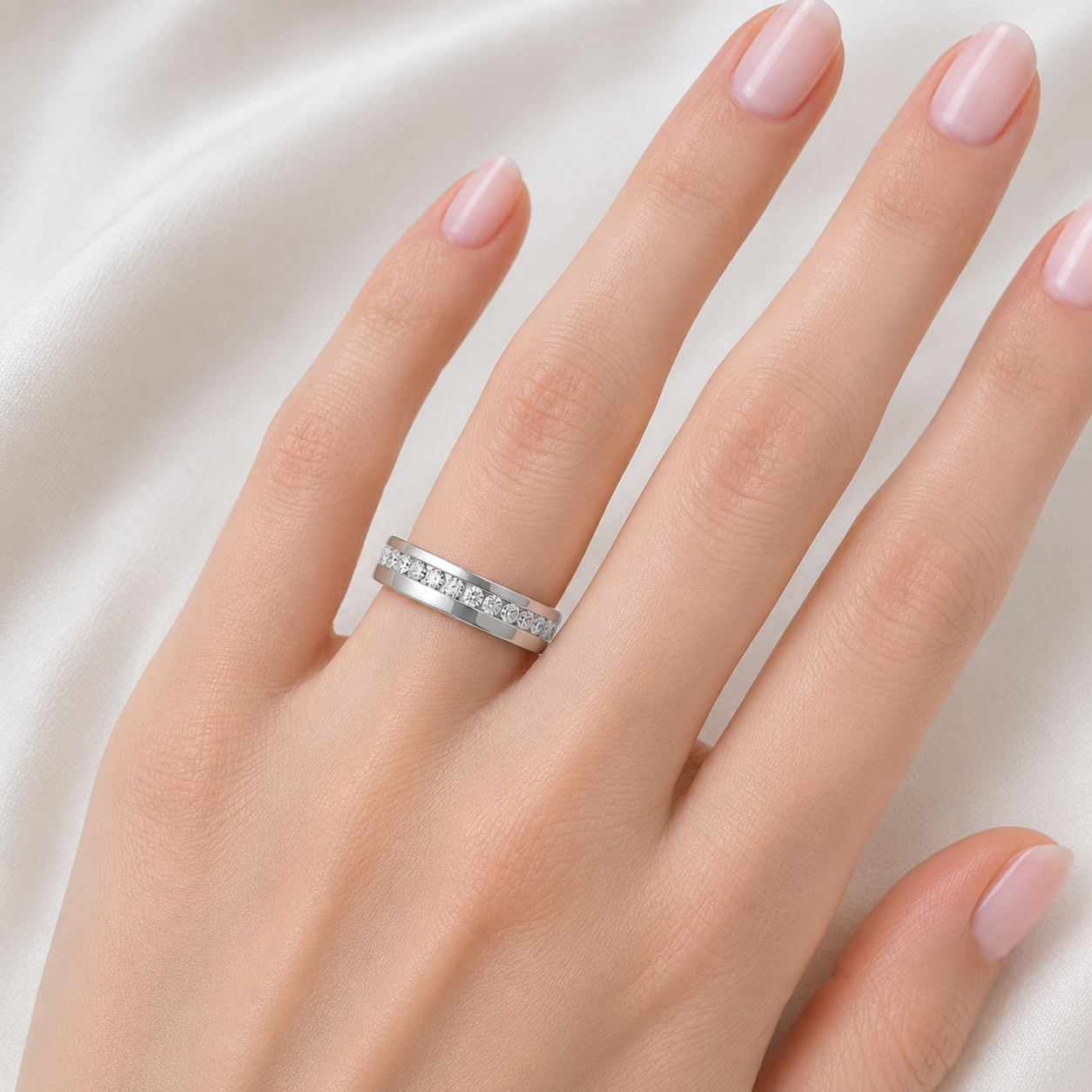 A close-up of a hand wearing a silver band ring set with small clear stones, photographed against a soft white fabric background.