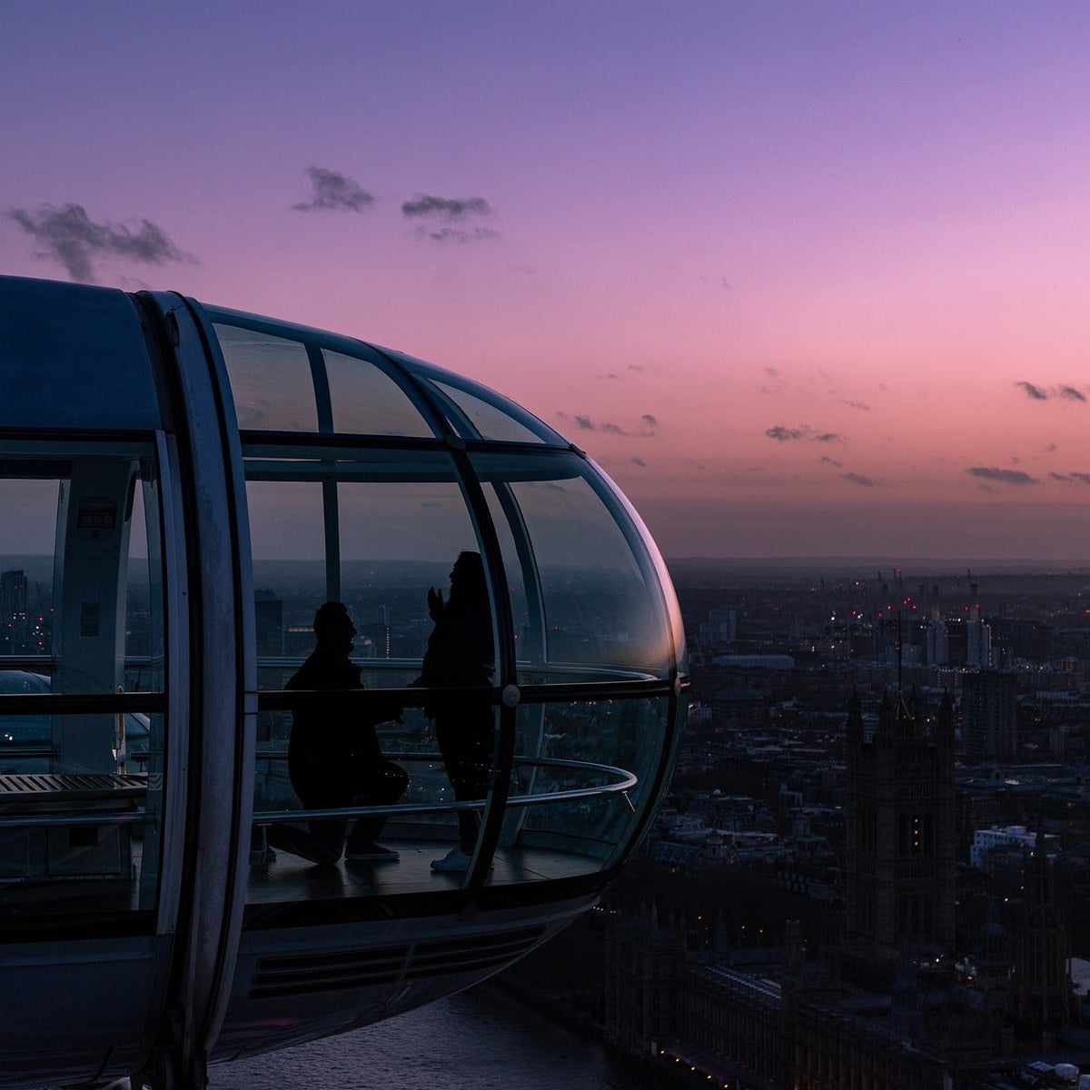 a proposal on the london eye, with silhouetted people standing inside and a city skyline under a pink and purple sky outside.