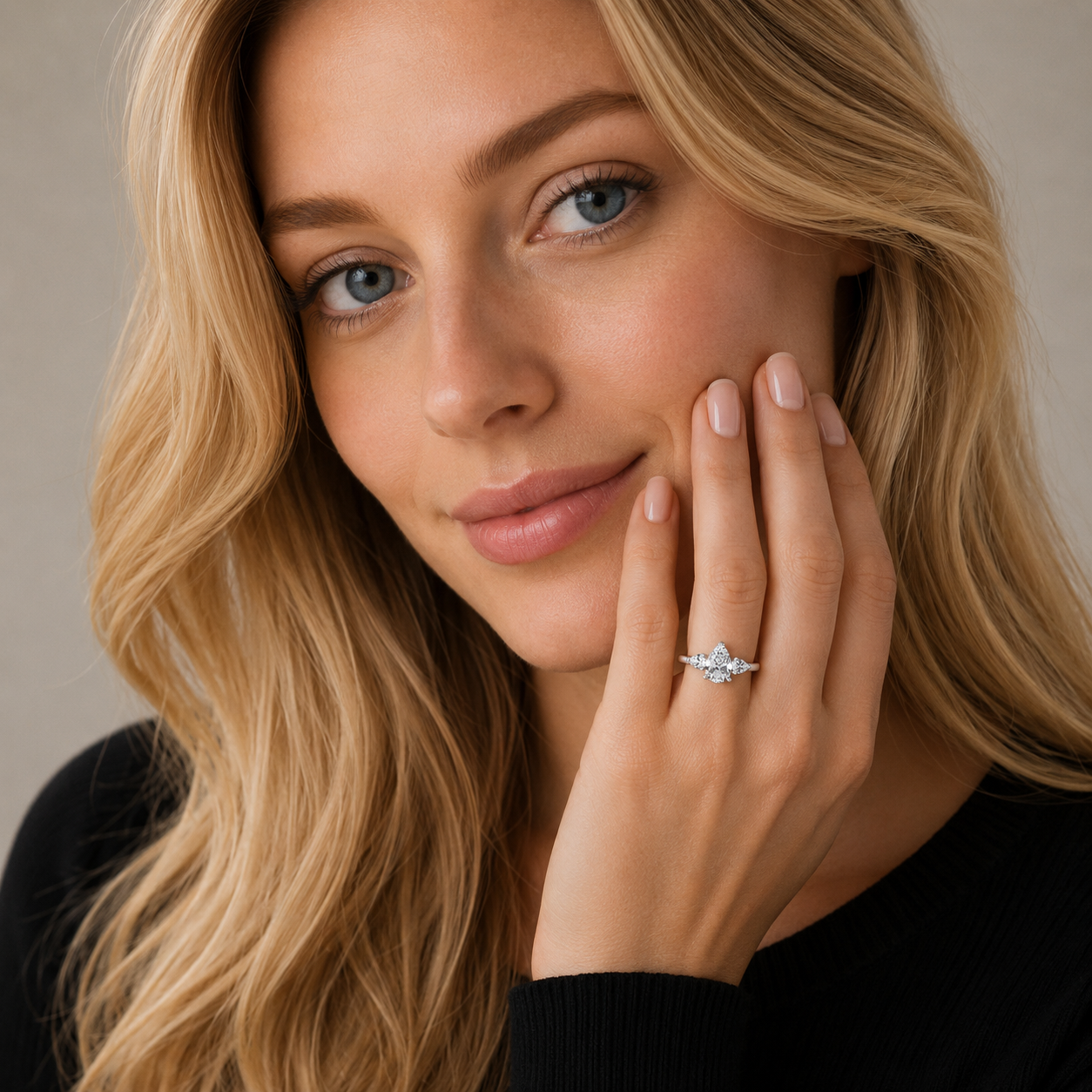 A close-up lifestyle shot of a woman with blonde hair wearing a delicate silver ring with a small clear gemstone on her finger, posing with her hand near her face against a soft beige background.