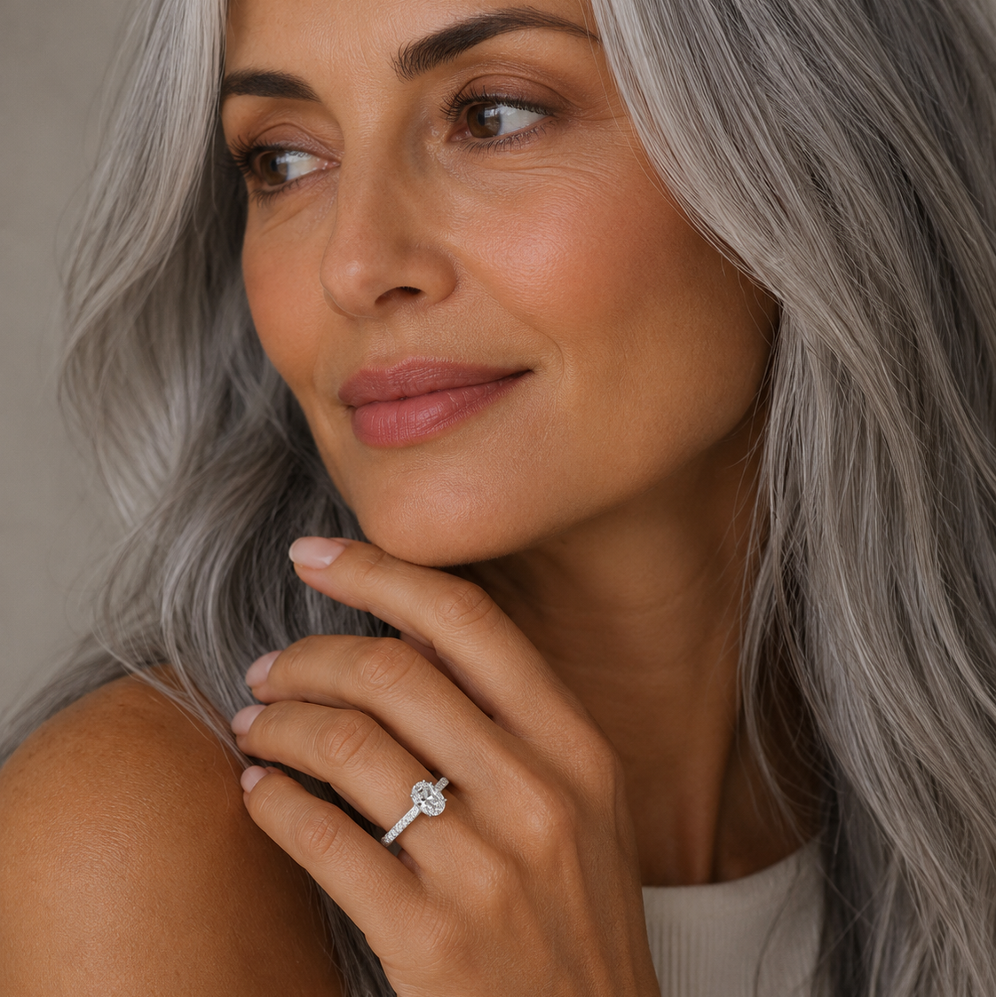 Woman with gray hair wearing a ring, against a neutral background