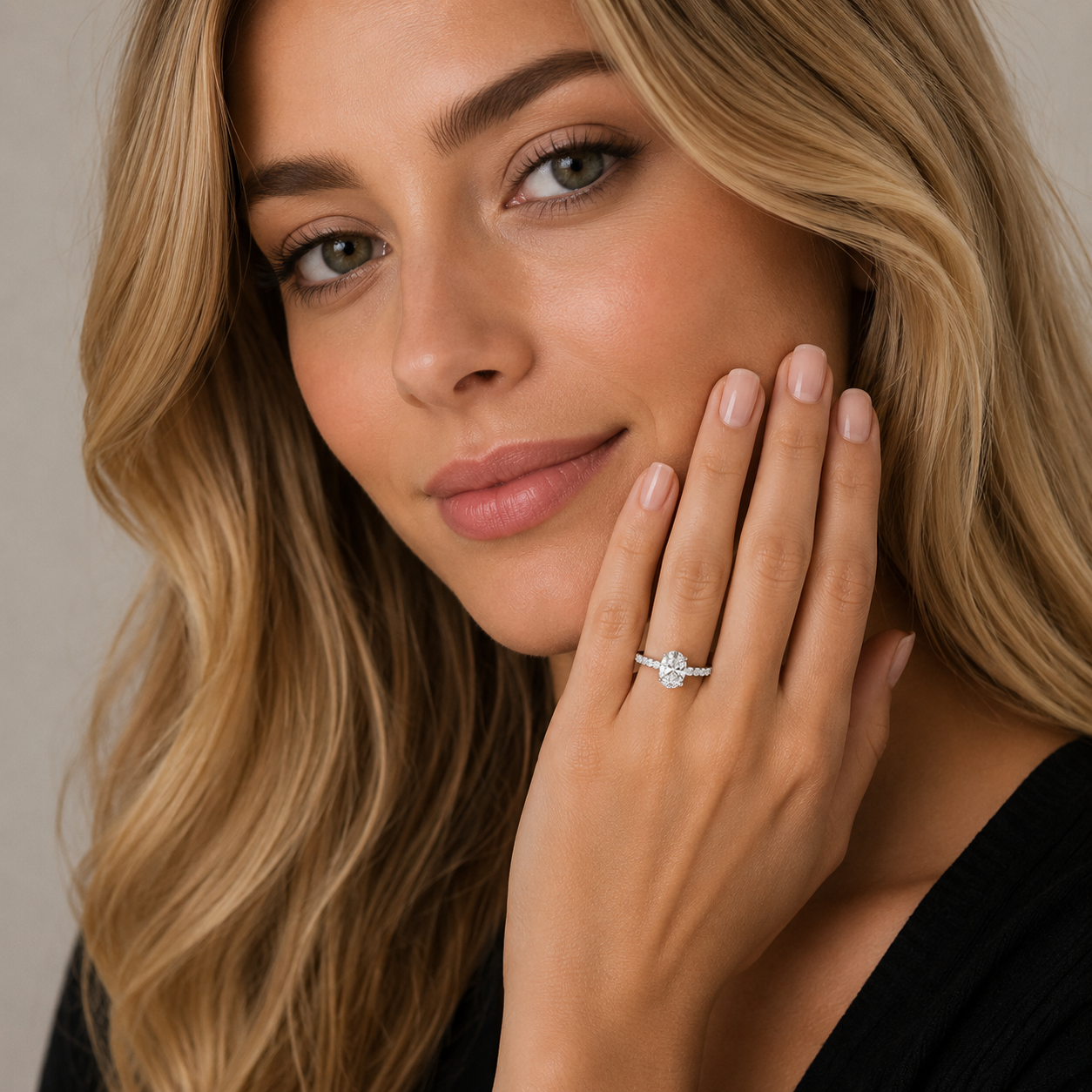 A close-up lifestyle shot of a woman with blonde hair wearing a silver engagement ring with a round-cut center stone and small side stones, resting her hand on her cheek.