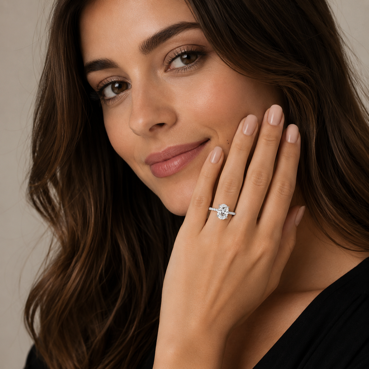 A close-up lifestyle shot of a woman with long brown hair wearing a silver-toned diamond engagement ring on her finger, with her hand resting against her cheek.