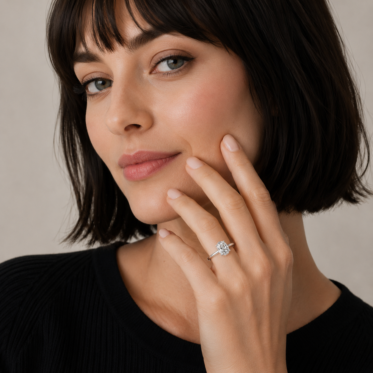 Woman wearing a ring with a diamond, touching her face against a neutral background