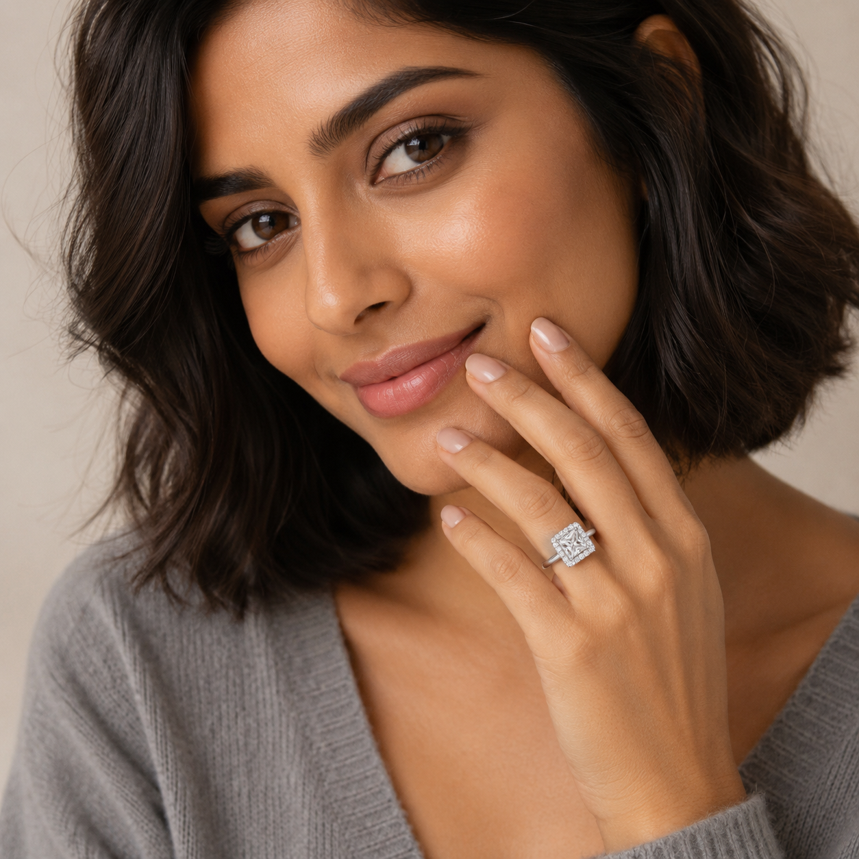 Woman wearing a diamond ring, posing with hand near face against a neutral background