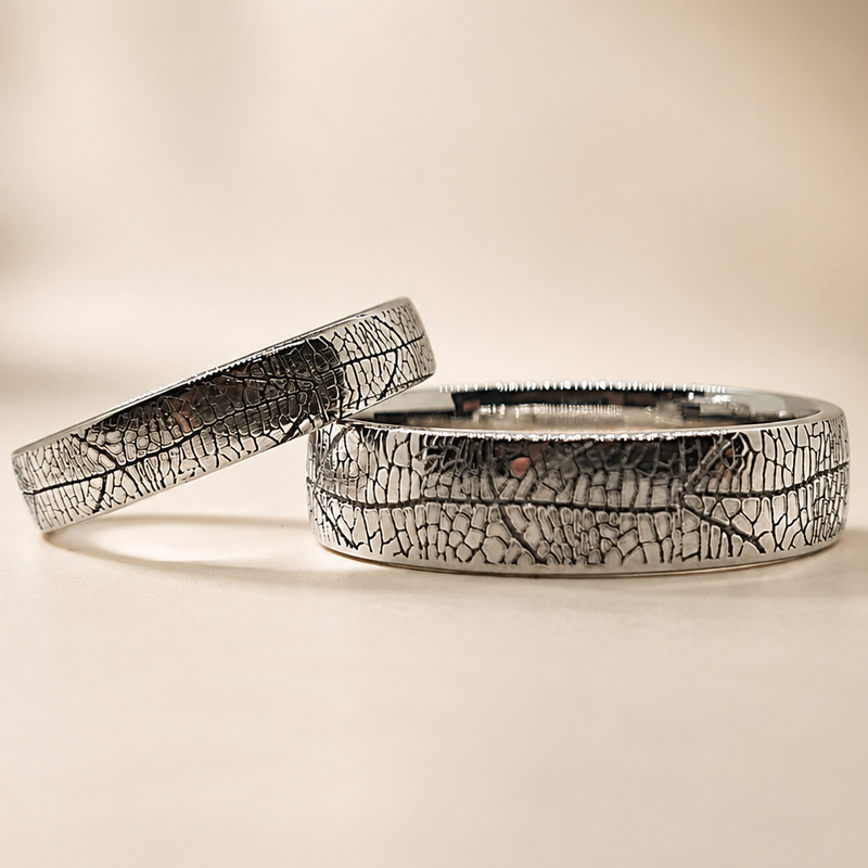 Two textured silver rings with a leaf-like crackle pattern, displayed on a warm beige background.