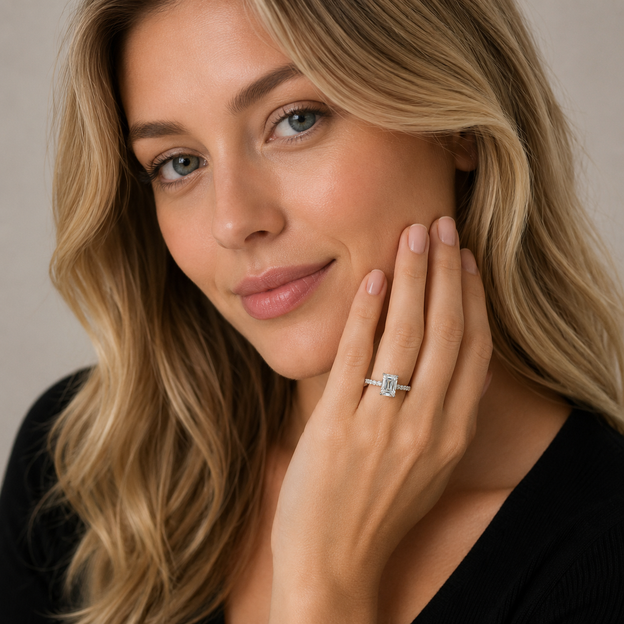 A close-up lifestyle shot of a woman with blonde hair wearing a silver ring with a square-cut clear gemstone on her finger, posing with her hand near her face against a soft beige background.