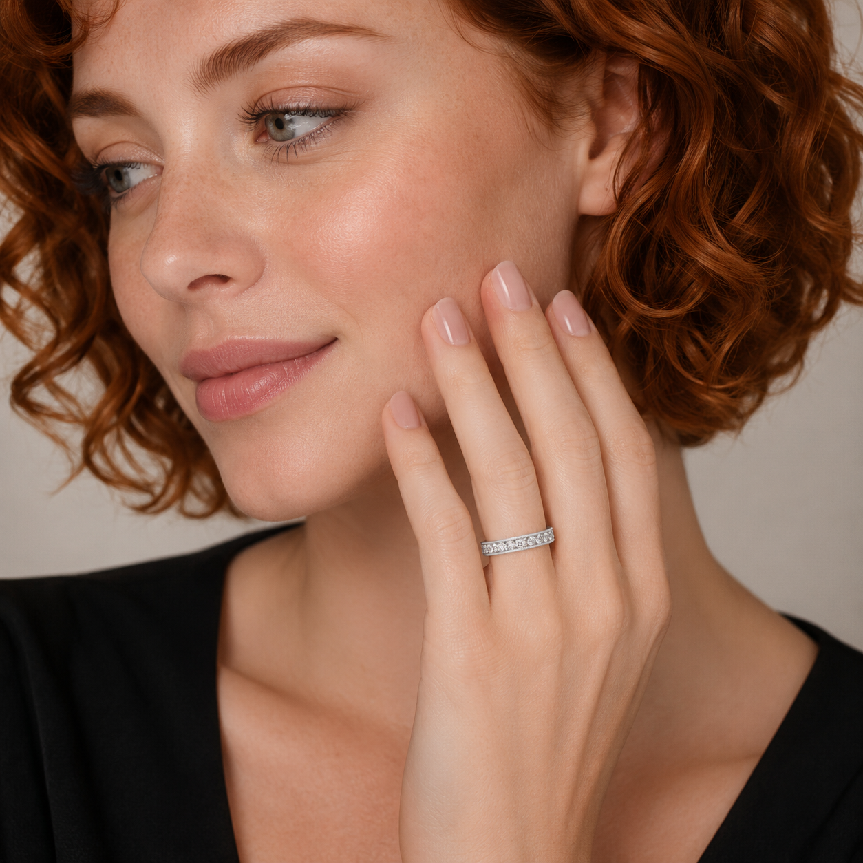 A close-up lifestyle shot of a woman with curly red hair wearing a thin silver band ring set with small clear stones on her ring finger.