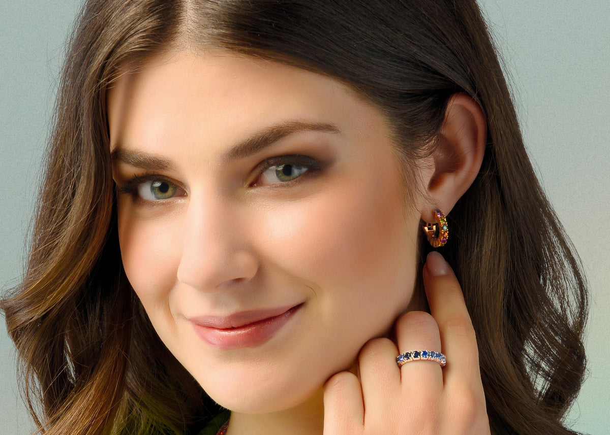 Woman wearing jewelry including earrings and a ring, with a neutral background