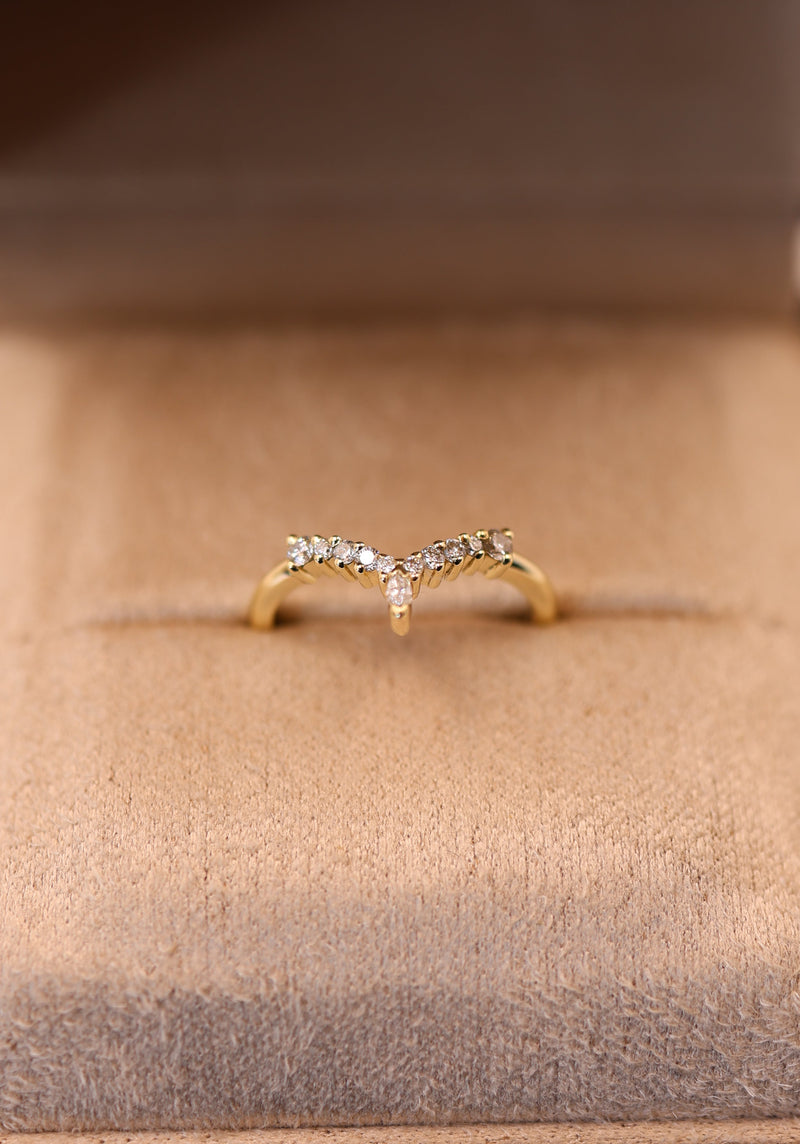 A delicate gold ring with small clear stones, displayed in an open dark brown jewelry box with a beige velvet interior.