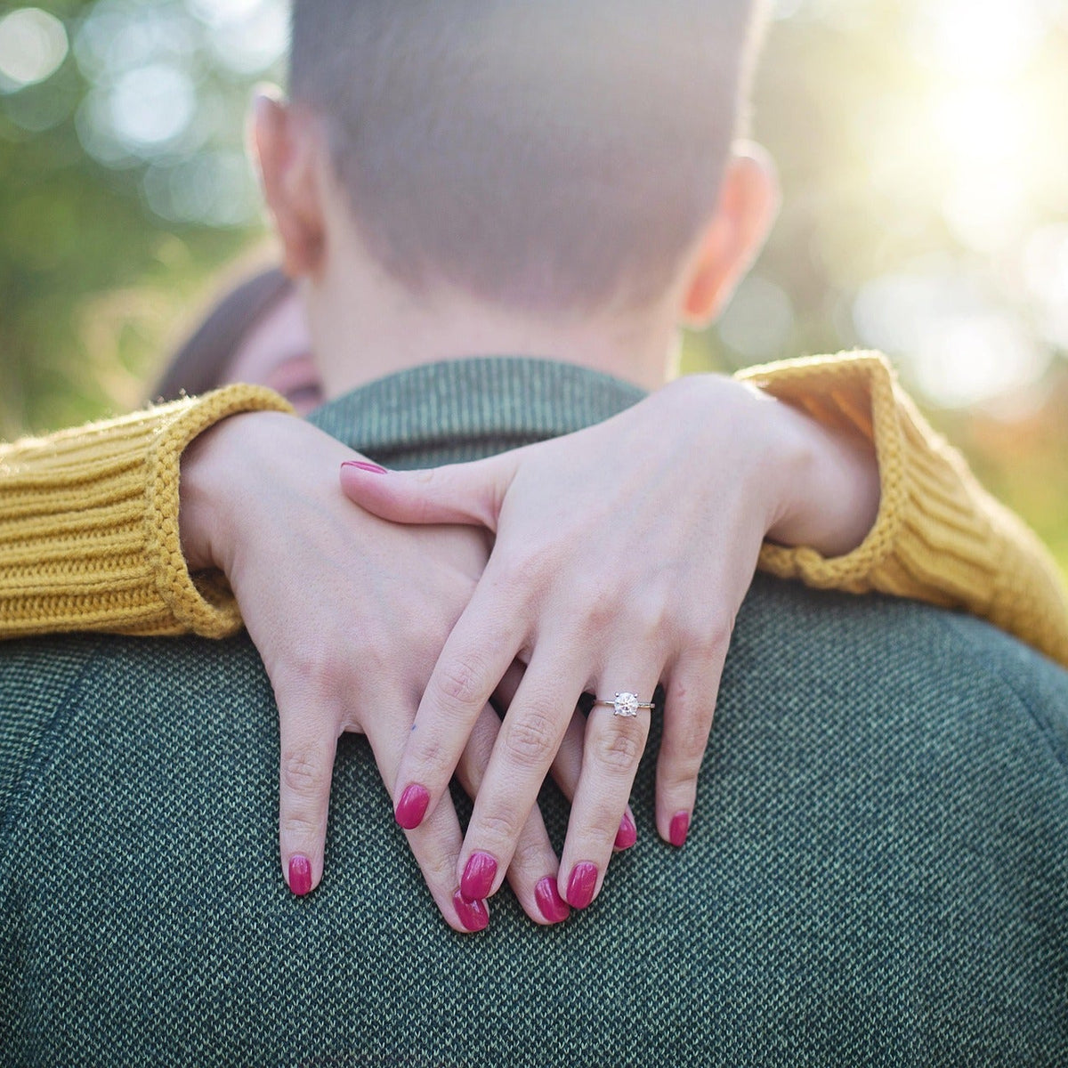 Person with a yellow sweater embracing another person outdoors with a blurred natural background