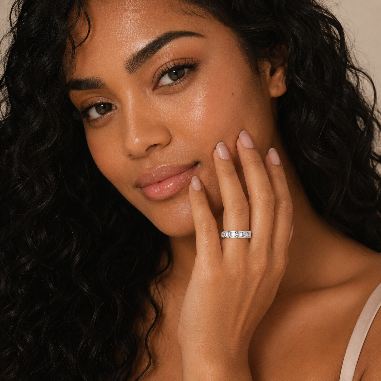 A close-up lifestyle shot of a woman with long, dark curly hair wearing a silver band ring on her ring finger. The ring features small, clear gemstones set in a row.