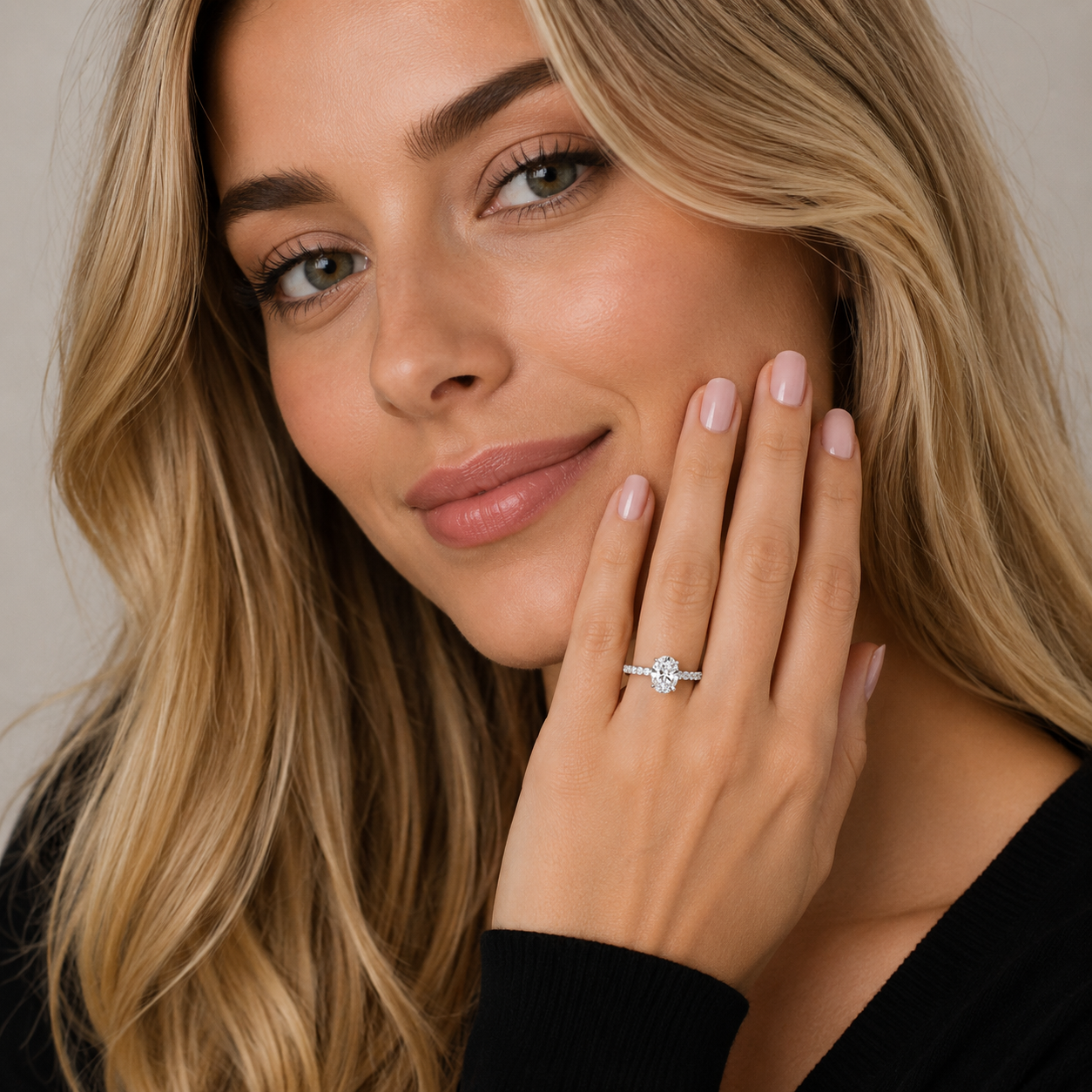 A close-up lifestyle shot of a woman with blonde hair wearing a delicate silver ring with a single round-cut clear gemstone on her finger, posing with her hand near her face against a soft neutral background.