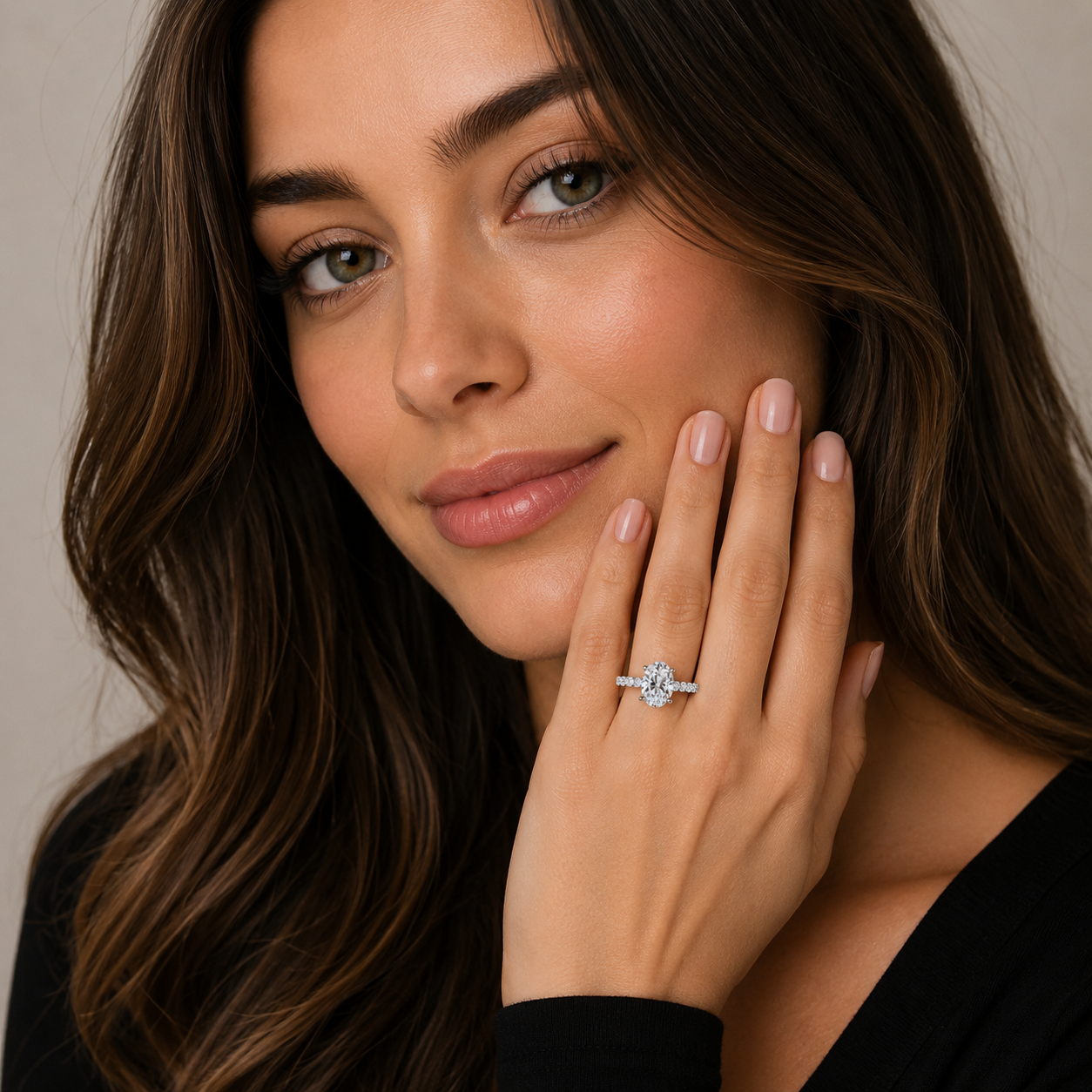 A close-up lifestyle shot of a woman with long brown hair wearing a silver-toned engagement ring with a round-cut clear gemstone on her finger, with her hand resting against her cheek.