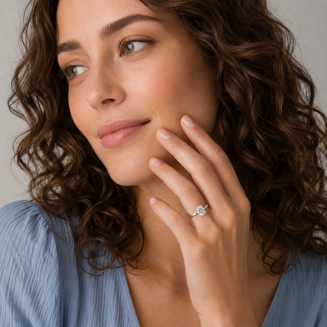Woman wearing a diamond ring, touching her face with a neutral background