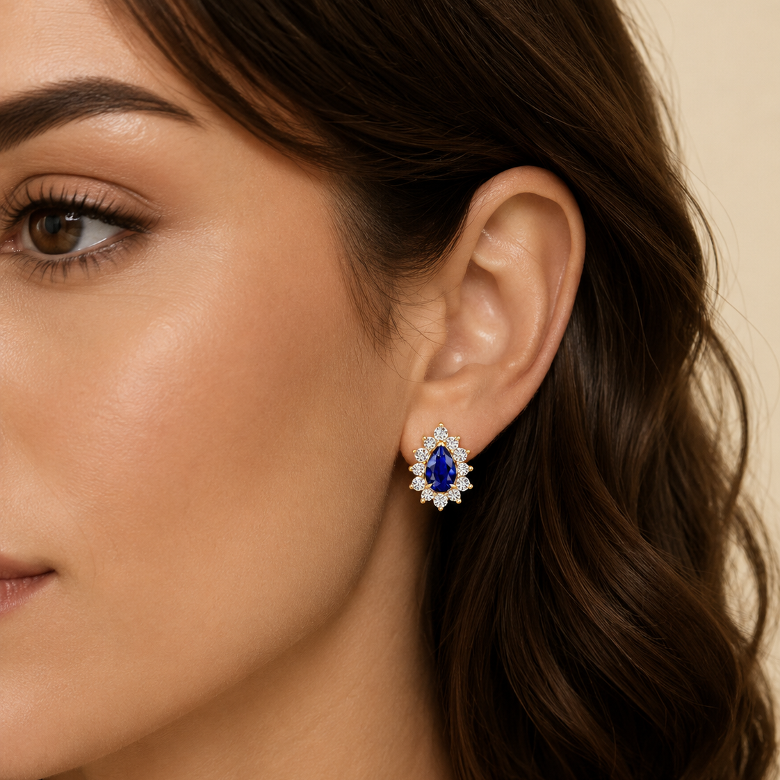 A close-up of a woman's ear wearing a single stud earring with a deep blue marquise-shaped center stone surrounded by small clear stones in a silver-toned setting.