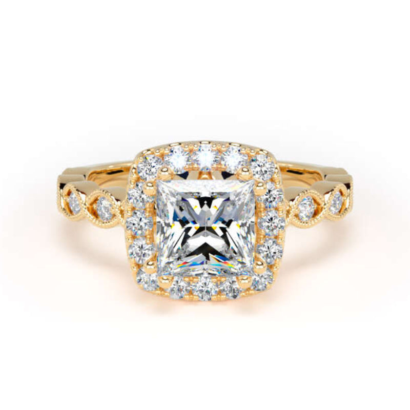 A yellow gold halo ring featuring a central princess-cut clear gemstone surrounded by a double halo of smaller round stones, with additional accent stones along the band, set against a plain white background.