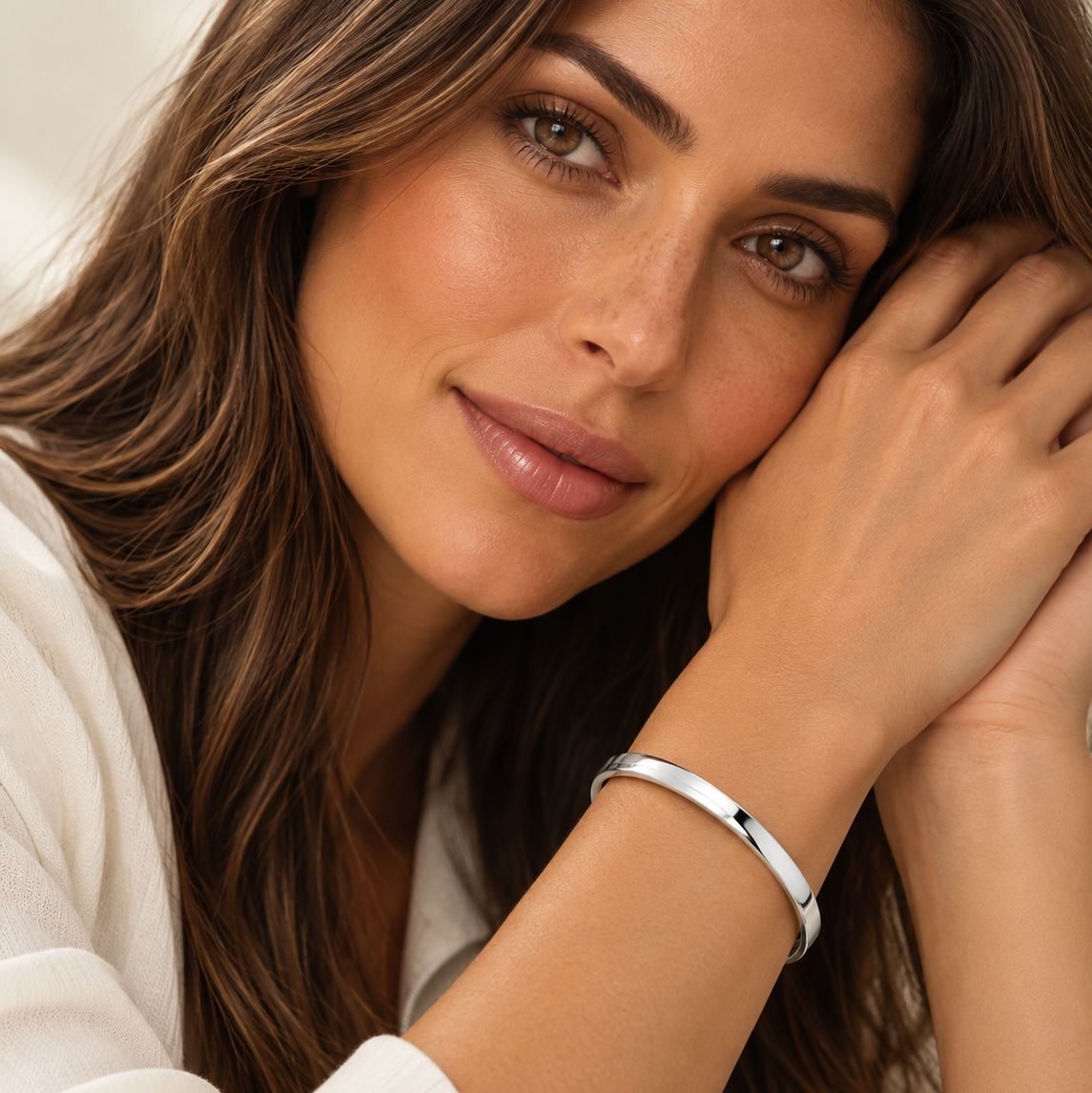 A close-up lifestyle shot of a woman with long brown hair wearing a polished silver bangle bracelet with a small black star detail, resting her head on her hand.