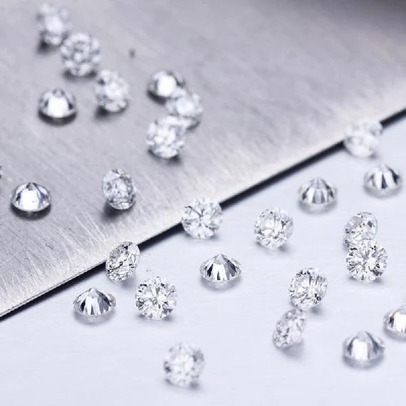 Multiple clear round-cut gemstones scattered across a brushed silver metal surface and white background.