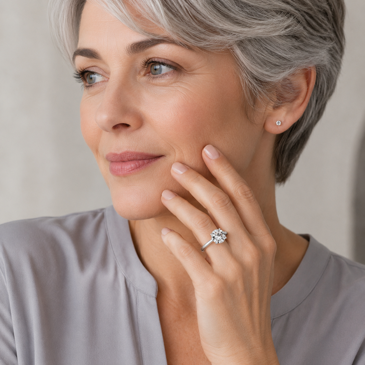 Woman wearing a diamond ring, touching her face with a neutral background